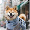 Un perro Shiba Inu peludo vistiendo un impermeable azul de doble capa y arnés, caminando al aire libre.