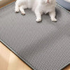 Eine weiße Katze steht auf einer grauen, strukturierten Unterlage auf einem hellen Holzfußboden.