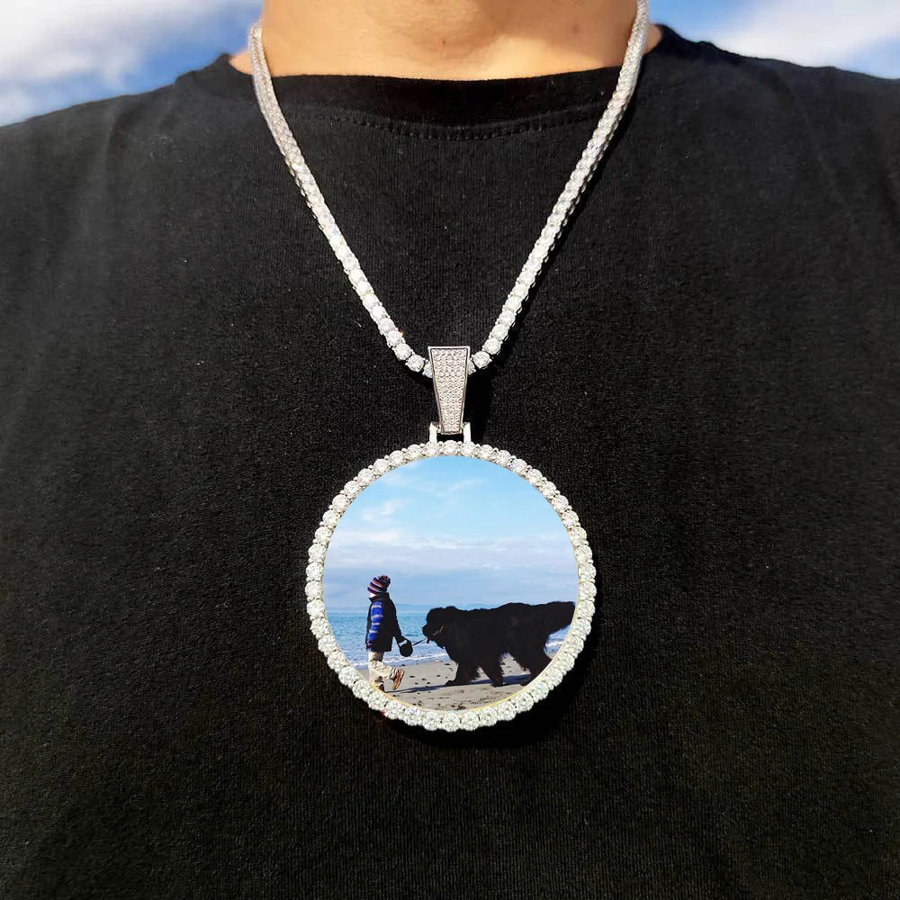 A silver chain necklace features a circular pendant depicting a silhouette of a person and a black bear on a beach.