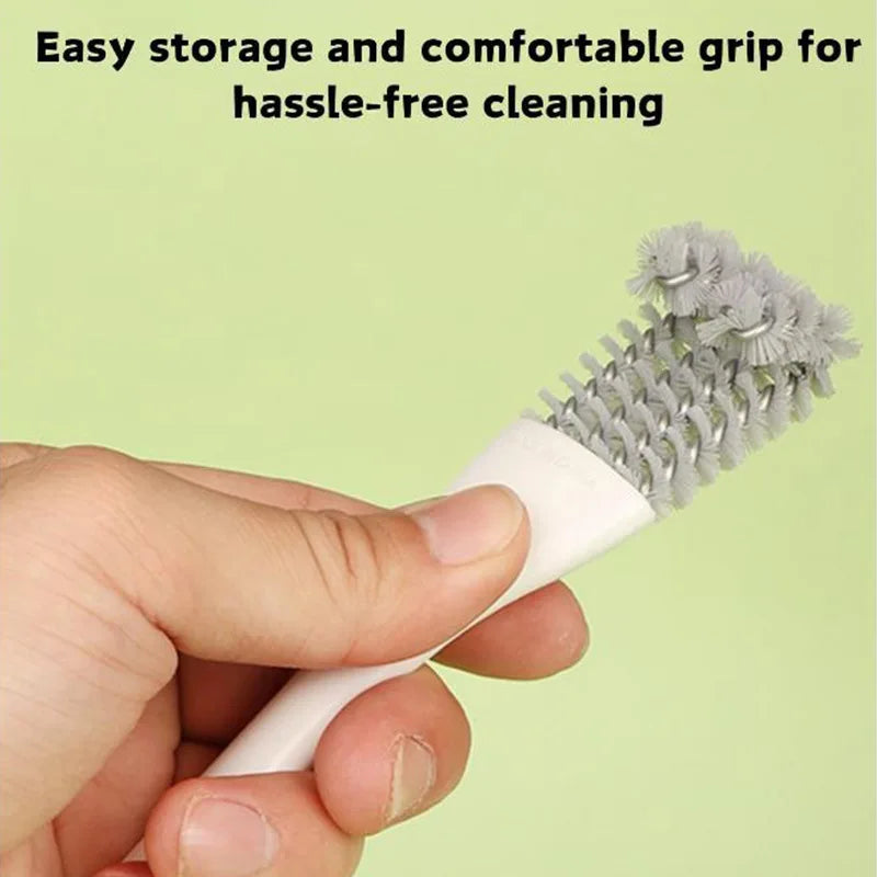 Una mano sostiene un cepillo de limpieza blanco con cerdas grises, diseñado para fácil almacenamiento y agarre cómodo.
