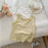 A pale yellow knitted mini vest for a baby girl with lace trim, resting on a white surface next to pink flowers.