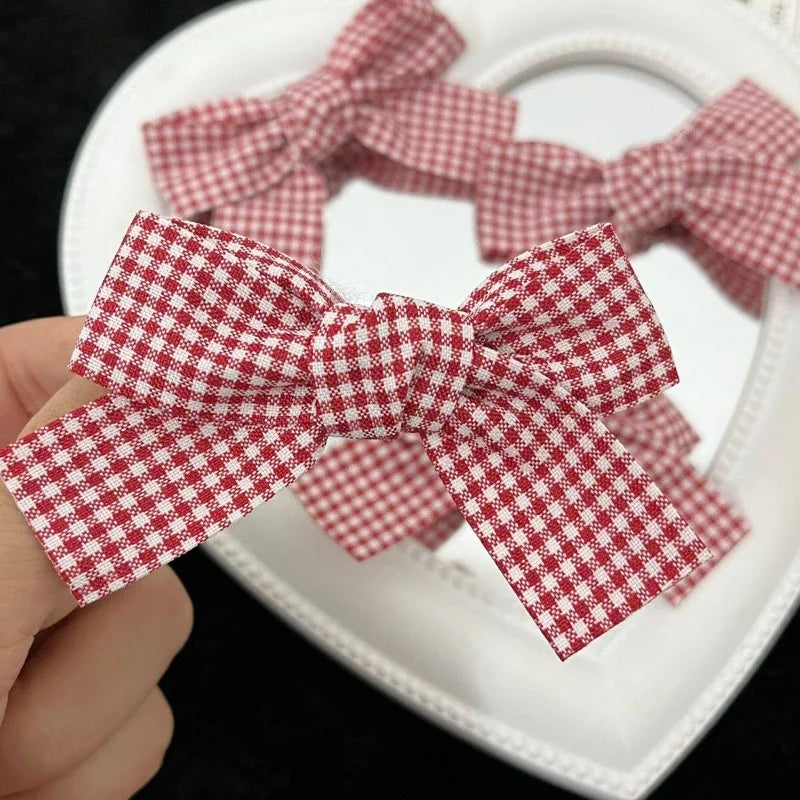 A hand holds a red plaid fabric bow used as hair clips for girls.