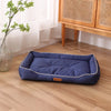 A navy blue waterproof orthopedic dog bed placed on a light wood floor next to a window and wooden furniture.