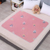 A pink patterned waterproof cartoon bed protector pad is placed on a light-colored table with a white pillow and a stuffed an