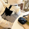 A white knitted dog dress with a black lace bow detail is displayed on a table.