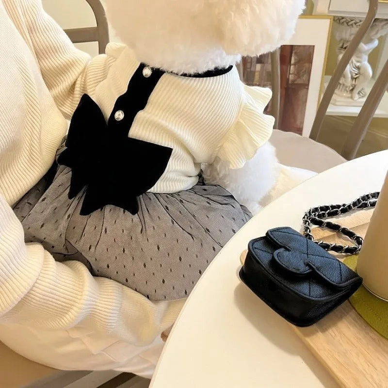 A white knitted dog dress with a black lace bow detail is shown on a table.