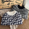 A black and white knit sweater featuring a repeating dog silhouette pattern is displayed on a wooden background.