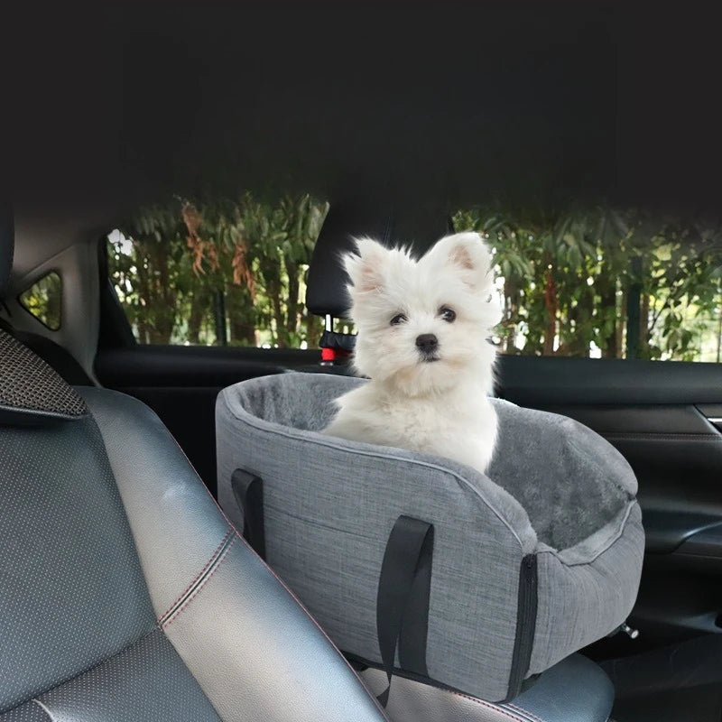 A small white dog is resting in a gray portable pet car bed with safety straps inside a car.