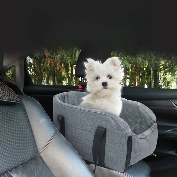 A small white dog is resting in a gray portable pet car bed with safety straps inside a car.