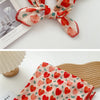 Gros plan d'un foulard en coton floral rouge et rose noué en nœud, exposé sur un fond en bois.