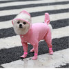 Un petit chien blanc portant un imperméable rose et des bottes assorties sur une surface rayée noir et blanc