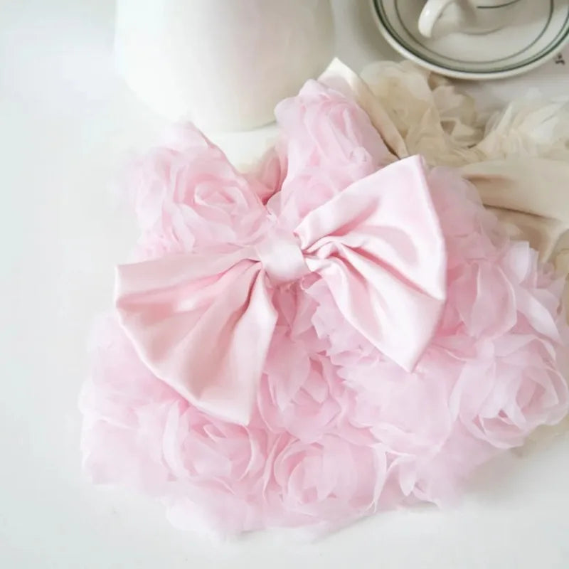 Vestidos para mascotas florales rosas con tela fruncida y un lazo, mostrados sobre una superficie blanca.