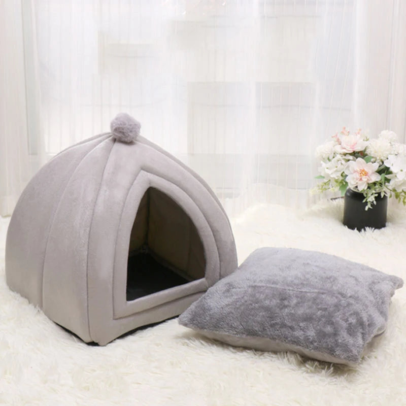 A gray cozy cat bed cave with a washable cushion resting on a white fluffy surface.