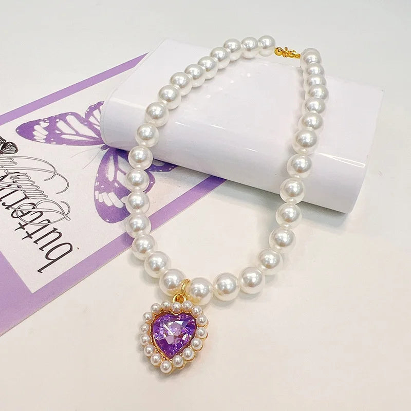 A delicate pearl necklace with a purple heart pendant displayed on a white background.