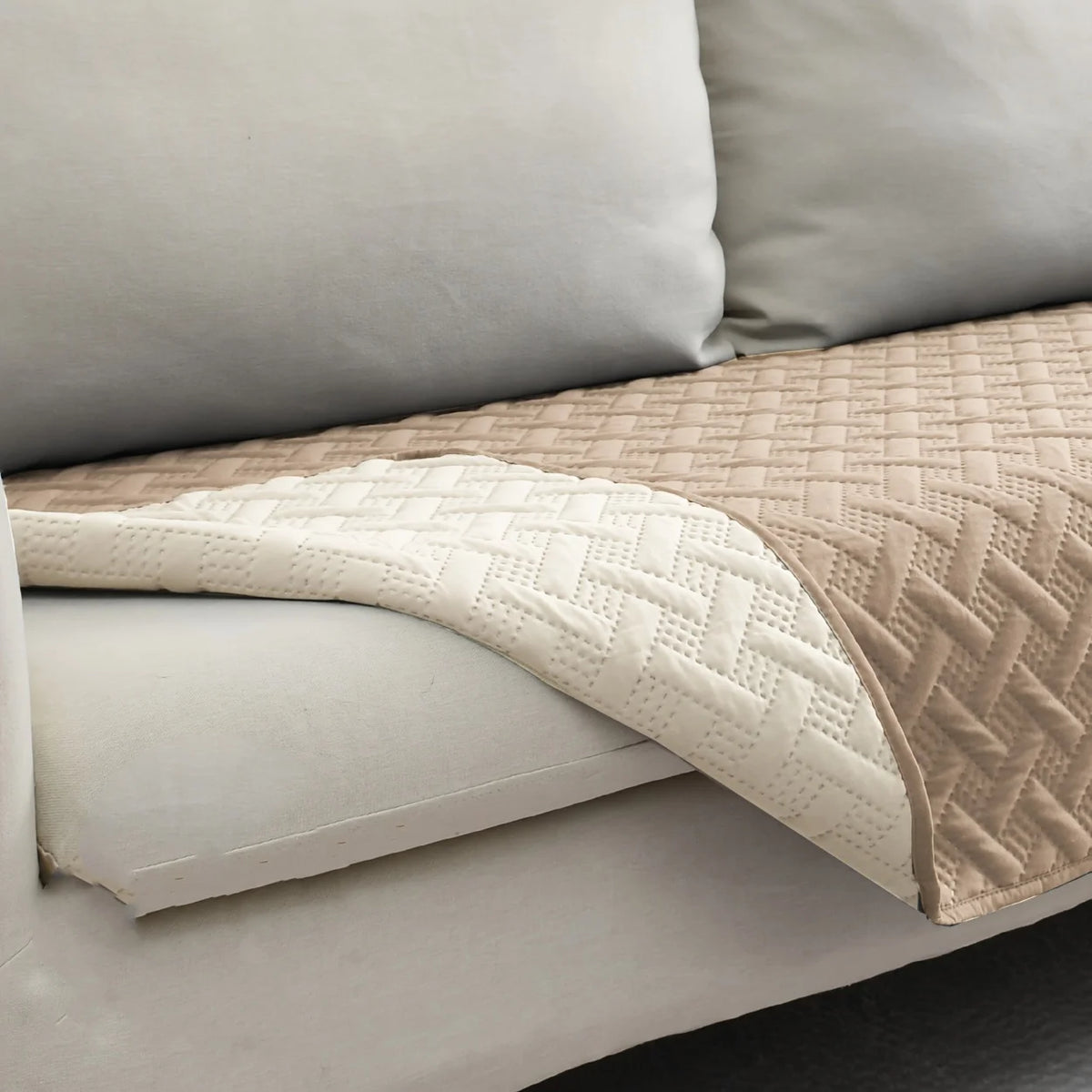 A beige quilted pet mat with a white border is shown resting on a light gray sofa cushion.