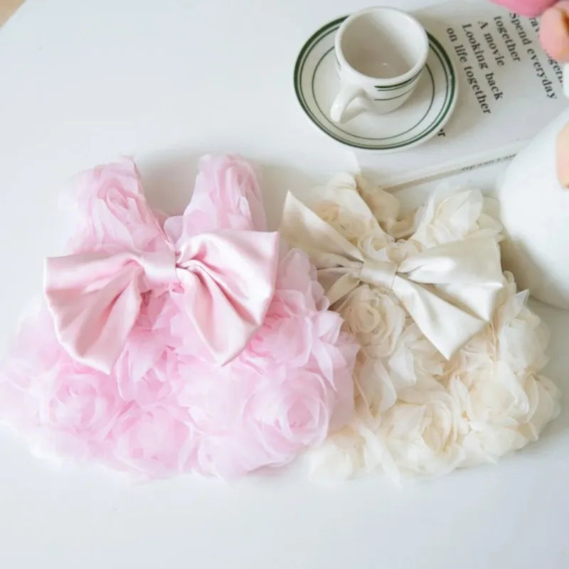 Vestidos florales rosas y crema para mascotas exhibidos junto a una taza y un cuaderno.