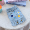 A light blue denim jacket for dogs decorated with colorful fabric flowers and a silver ring detail.