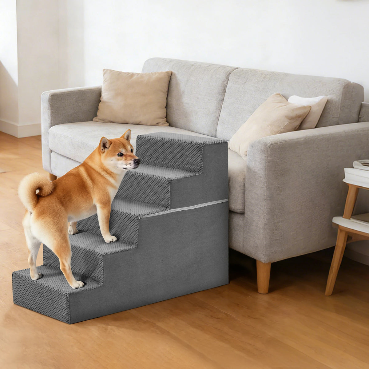 A dog stands on a gray adjustable climbing stairs ramp placed in front of a light gray sofa.