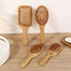 Three wooden bamboo hair brushes with massage bristles are displayed on a wooden surface.