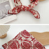 Une écharpe en coton à motif floral rouge et crème est présentée à côté d'un objet en bois clair.