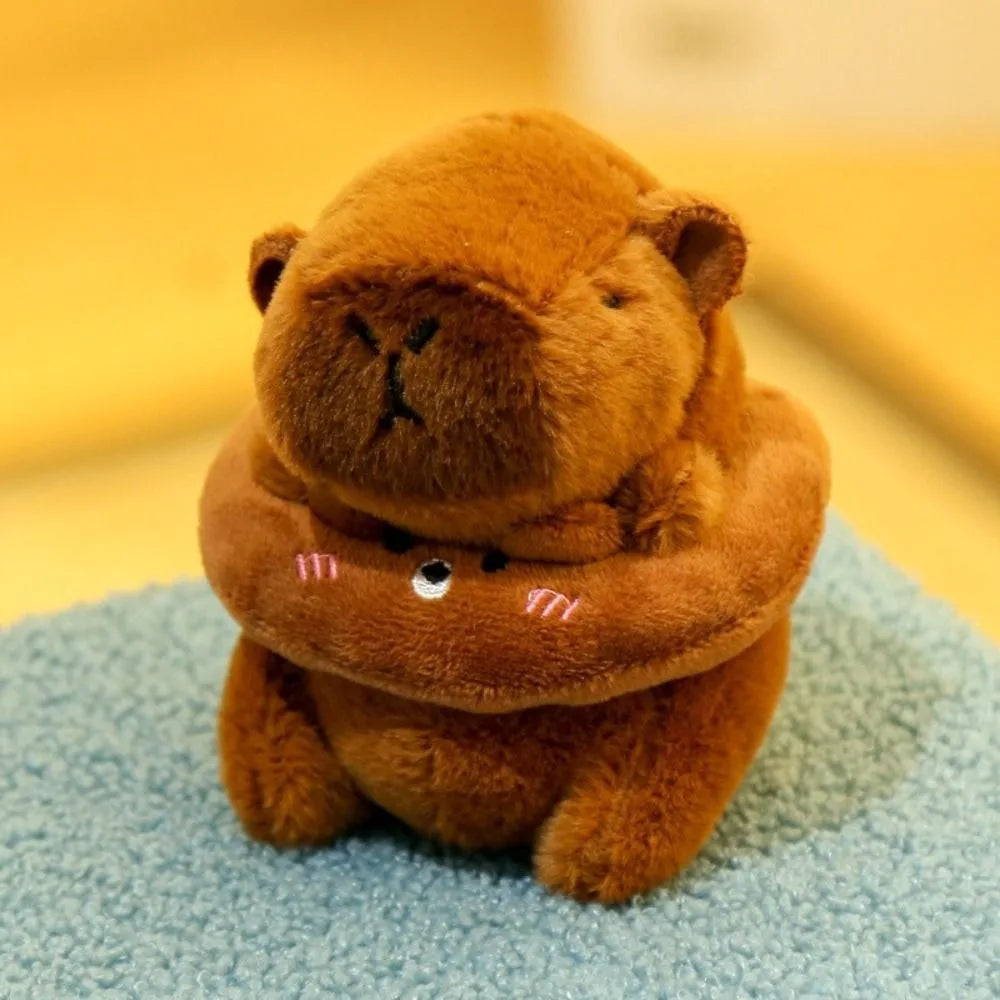 A fluffy brown capybara plush doll wearing a hoodie with small wings, sitting on a light blue surface.