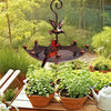 An antique umbrella bird feeder with a bath bowl featuring a dark metal bird silhouette and green foliage.