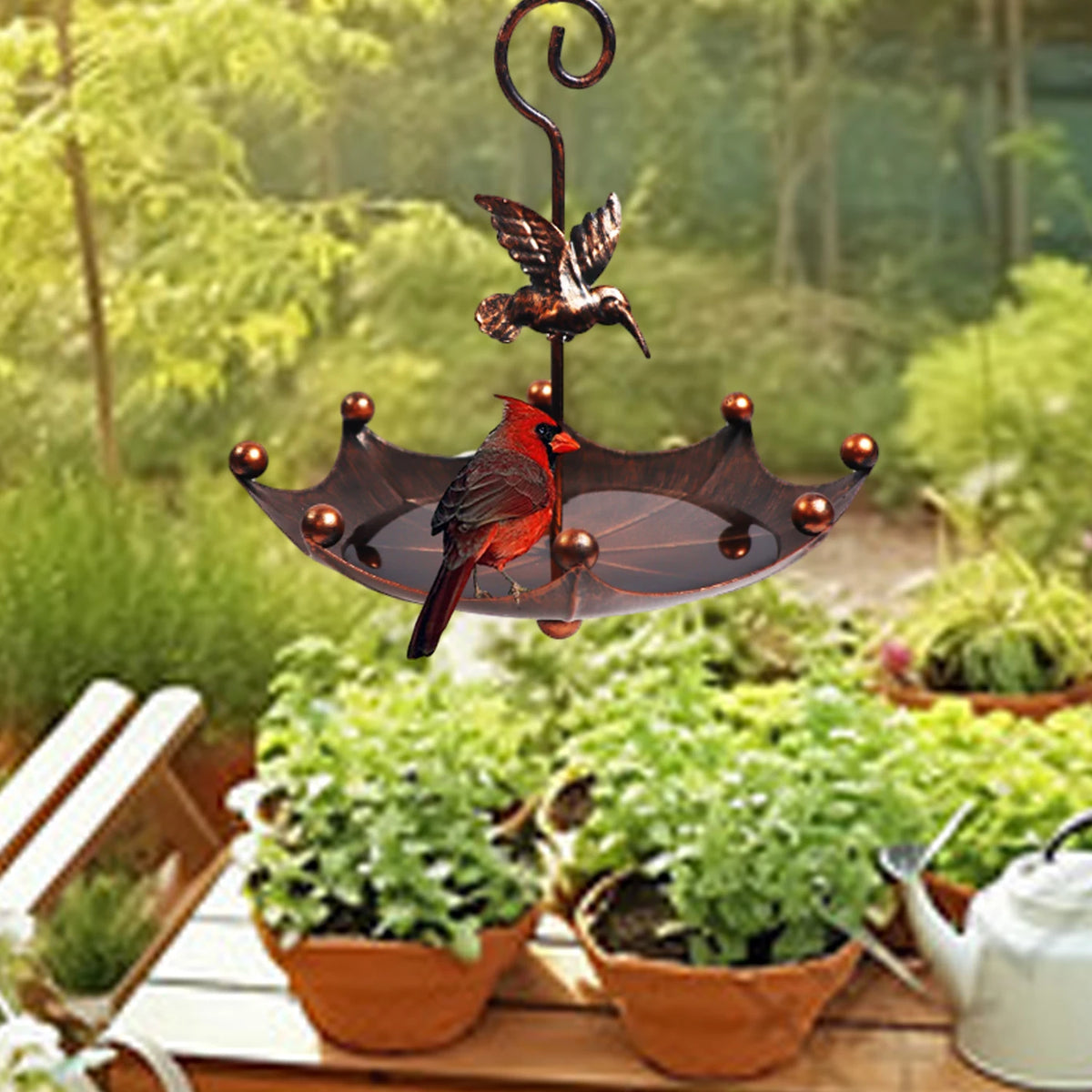 An antique umbrella bird feeder with a bath bowl featuring a dark metal bird silhouette and green foliage.