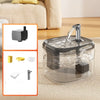 A clear glass cat drinking fountain with a metal spout is shown on a beige fabric surface.