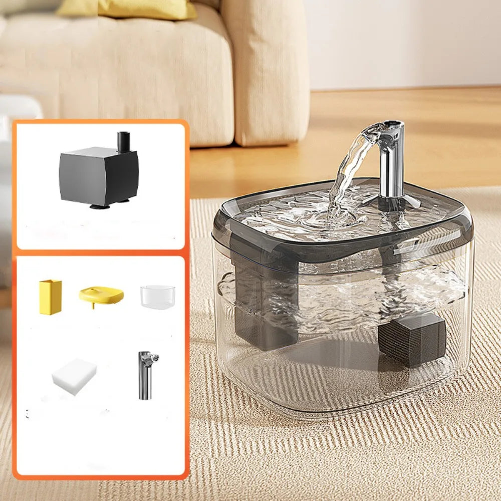A clear glass cat drinking fountain with a metal spout is shown on a beige fabric surface.