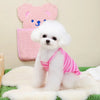 A fluffy white dog is sitting on a green mat in front of a pink bear-shaped towel.