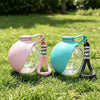 Zwei Glas-Wasserdispensierer mit rosa und türkisfarbenen Deckeln und schwarzen Riemen auf grünem Gras.