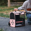 A pink ventilated bird travel backpack with a clear window and feeding cups is being held by a person outdoors.
