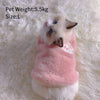A fluffy white and gray kitten wearing a pink embroidered vest on a white fur background.