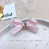 Pink satin bow hair accessory with rhinestone pearl accents displayed on a white plate.