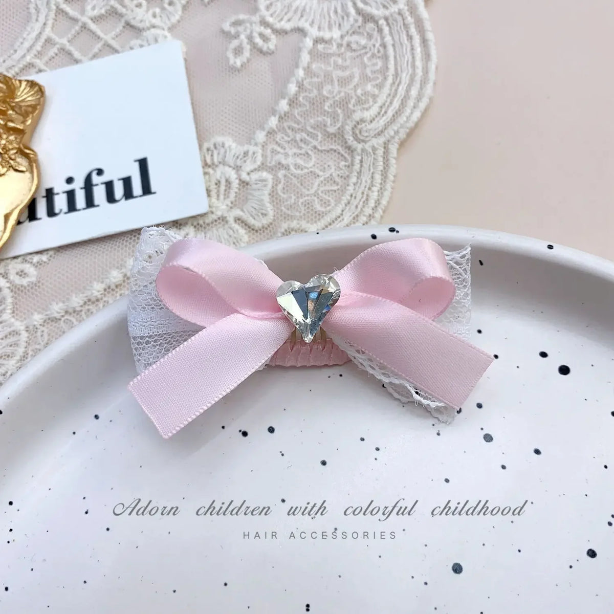 Pink satin bow hair accessory with rhinestone pearl accents displayed on a white plate.