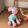 A handmade plush toy of a donkey with pink and blue fur sitting next to a wire basket.