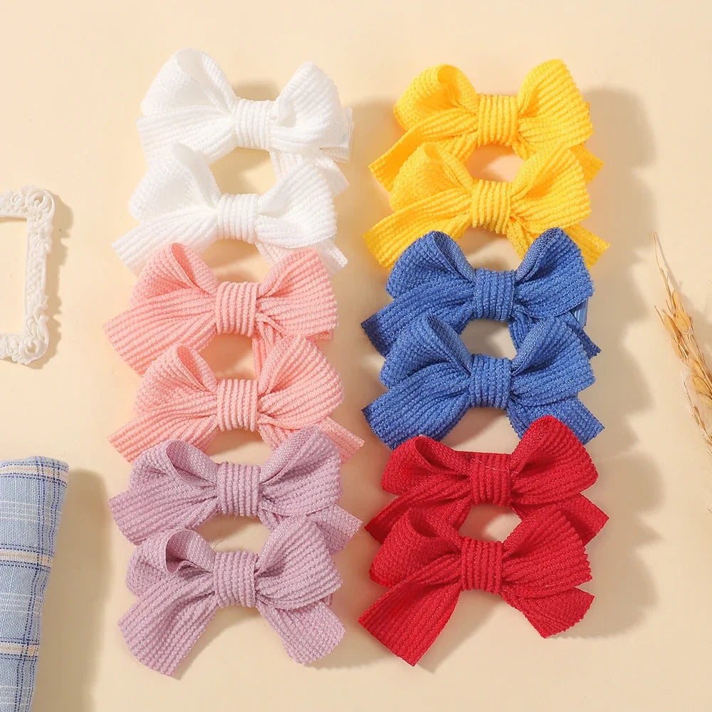 Collection de nœuds papillons en ruban de tissu colorés (blanc, jaune, rose, bleu et rouge) sur fond clair.