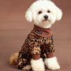 A fluffy white dog wearing brown leopard print pajamas.