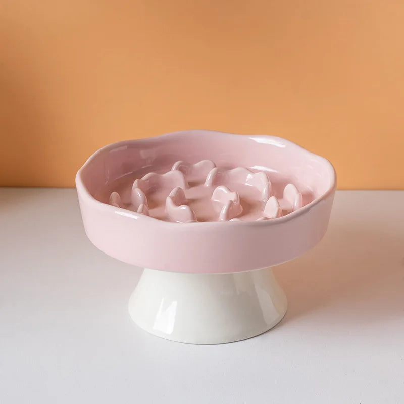 Bol en céramique rose à alimentation lente pour animaux sur un piédestal blanc sur fond orange.