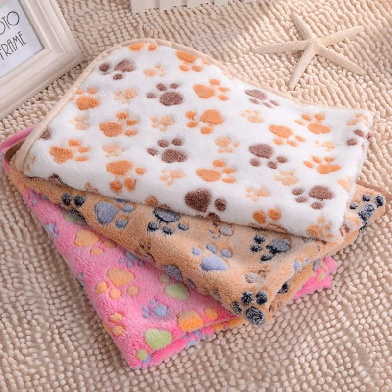 A stack of soft fleece pet bed mat covers featuring various paw print patterns in orange, white, and pink tones.