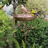 Vogelbad mit einer breiten, flachen Schale auf einem Metallständer in einem üppigen Garten.