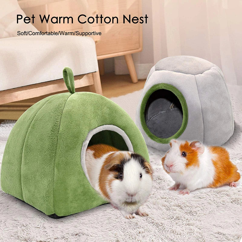 A green plush cave nest for a small rodent is shown next to a gray pet, resting on a white fluffy rug.
