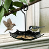 A black umbrella-shaped hanging bird feeder with seeds, featuring a small bird in flight.