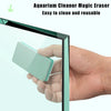 A hand holds a light green plastic eraser used to clean an aquarium glass.
