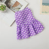A purple polka dot dog dress for small breeds with a ruffled skirt, displayed on a light surface.