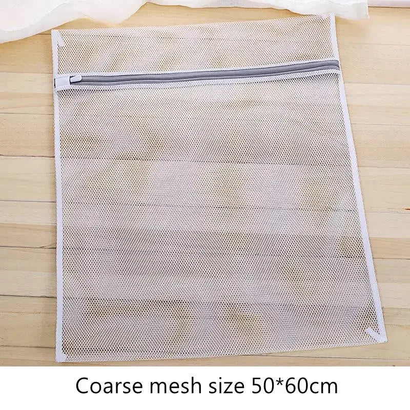 Bolsa de ropa reutilizable de malla blanca con cremallera sobre una superficie de madera.