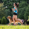 A woman is running outdoors with a golden retriever on a hands-free reflective dog leash.