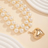 A delicate pearl choker necklace with a heart pendant displayed on a light background.
