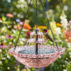 Rosa Glasvogelbadbrunnen mit mehrstufigem Wasserfeature und einem kleinen Vogel, draußen aufgehängt.
