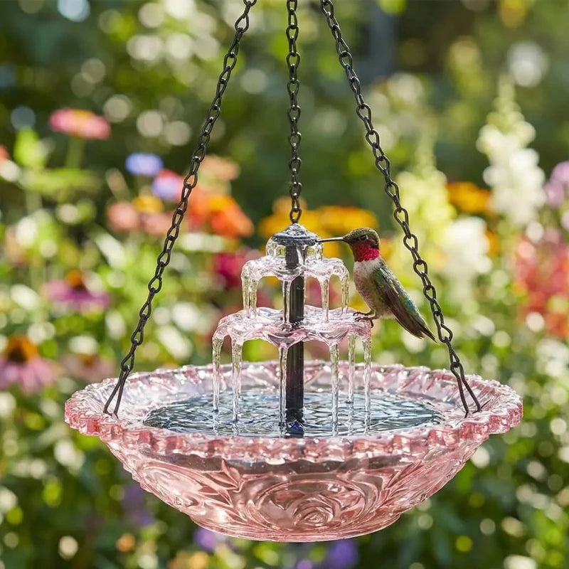 Rosa Glasvogelbadbrunnen mit mehrstufigem Wasserfeature und einem kleinen Vogel, draußen aufgehängt.